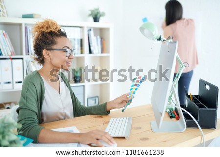 Portrait of smiling African woman choosing color scheme and holding swatches while working at desk in modern design studio, copy space