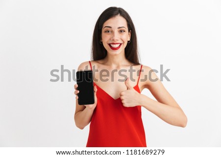 Portrait of a happy young woman in dress isolated over white background, showing blank screen mobile phone