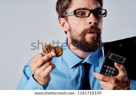 A surprised man holds a Bitcoin crypto currency and a calculator                           