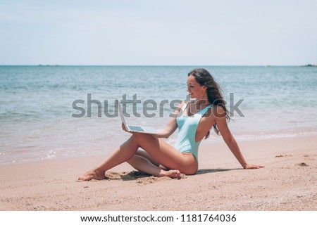 beautiful woman using laptop at the beach near the waves of blue on tropical beach background near ocean / Summer concept