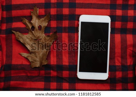 White mobile phone with autumn maple leaf with smile on red cell background