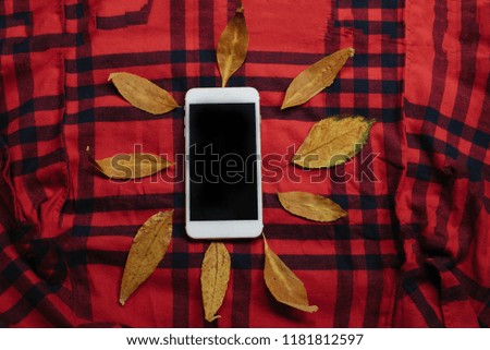 White mobile phone with autumn yellow maple leaf on red cell background