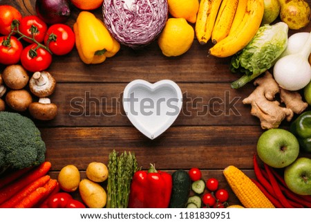 Top view of a wooden table full of vegetables and in the middle of the image an empty heart shaped dish, conceptual photo, food lover