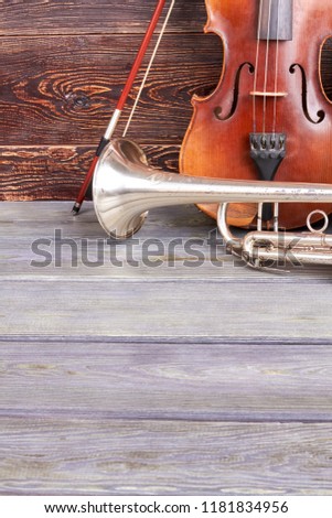 Orchestral musical instruments. Vintage style violin and trumpet on wooden background with copy space, vertical image.
