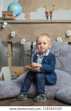 A Serious Baby sits on a big toy bear, dressed in a suit and holds a large book
