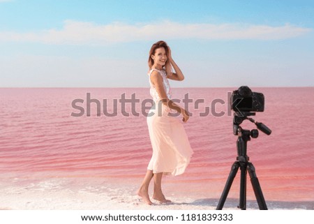Young woman posing in front of professional camera near pink lake on sunny day