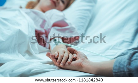 Recovering Little Child Lying in the Hospital Bed Sleeping, Her Hand Falls into Mother's and She Holds it Comfortingly. Focus on the Hands. Emotional Family Moment. Royalty-Free Stock Photo #1181842840