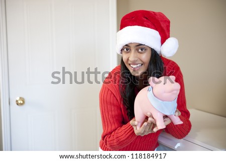 Portrait of happy girl with Christmas cap holding piggy-bank with her saving