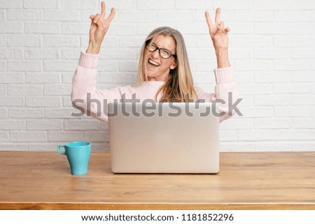 senior businesswoman with a proud, happy and confident expression; smiling and showing off success while gesturing victory with both hands, giving an "achiever" look, celebrating triumphantly.