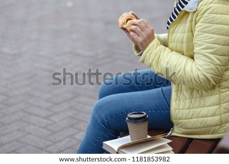Girl sitting on a wooden bench, reading a book and drinking coffee