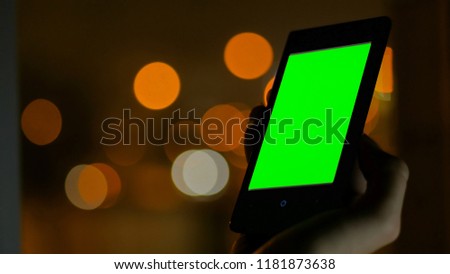 Woman looking at vertical smartphone with green screen at night. Blurred traffic bokeh light. Mock up and technology concept
