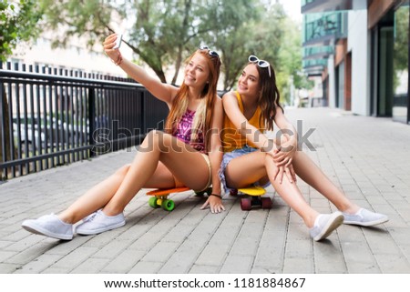 friendship, leisure and technology concept - happy teenage girls or friends with skateboards on city street taking selfie by smartphone in summer