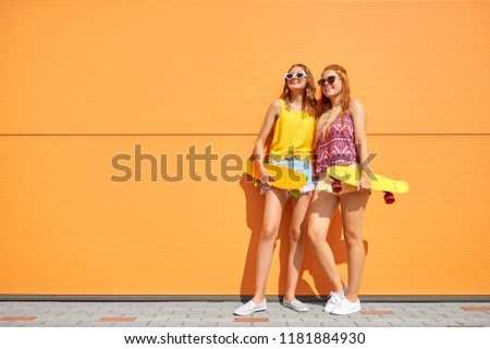 friendship, leisure and people concept - happy teenage girls or friends with short skateboards on city street in summer