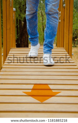 lower section of man in blue jeans and white sneakers walking on parquet floor with yellow arrow. 