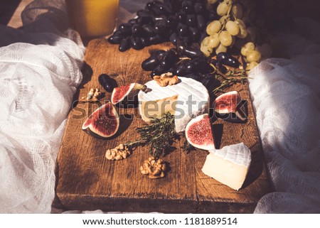 Cheese soft camembert with mildew on the branches of oregano on a dark wooden background with grapes, fig tree and walnuts