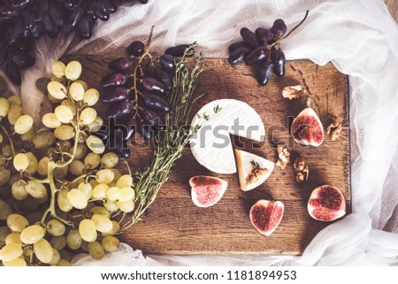 Cheese soft camembert with mildew and oregano branches on a dark wooden background with grapes, fig tree and walnuts. View from above