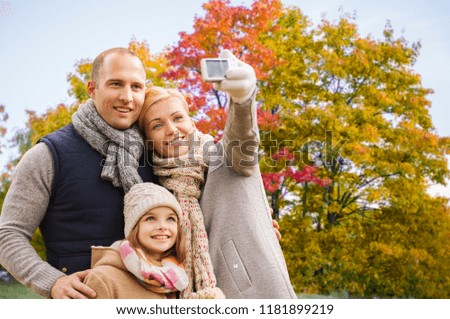 family, technology and people concept - happy mother, father and daughter taking selfie by camera over autumn park background