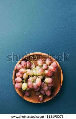 Bunch of red grape on wooden plate on dark blue background. Top view with copy space.