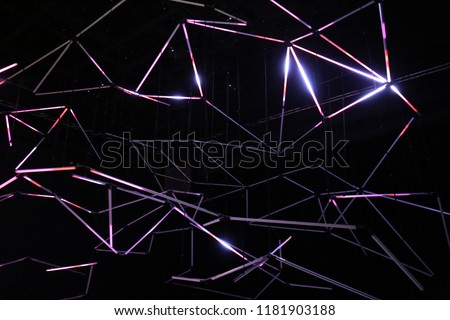 Indoor view of fluorescent neons in a dark dance hall. Pattern of white lines making polygonal shapes with a black background. Modern abstract design with drawings created by illuminated long lamps.