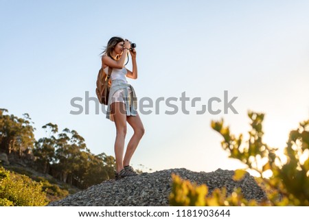 Female hiker taking pictures with digital camera from the top of a hill. Young woman capturing the images of beautiful landscape.