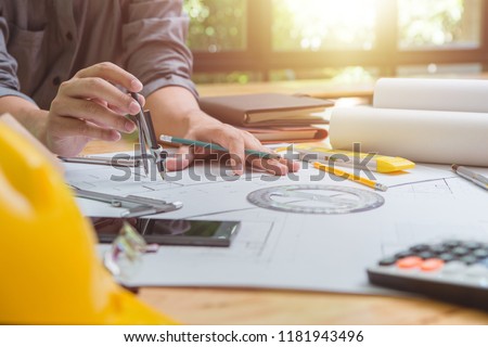 Hands of architect or engineer using drawing compass working with blueprint on desk in office .Engineering tools and construction concept.Architect and Business concept.Selective focus,Vintage effect.