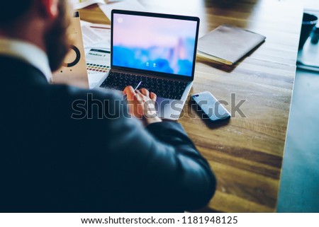 Back view of male entrepreneur using application on laptop computer for browse information on web page holding diagram for analysing, cropped image of financial expert prepare report via netbook
