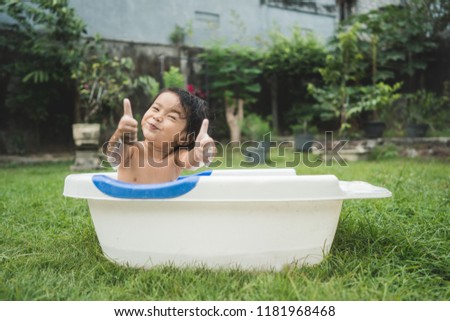 portrait of happy beautiful baby girl take a bath in a baby bath tube while giving thumbs up at home backyard