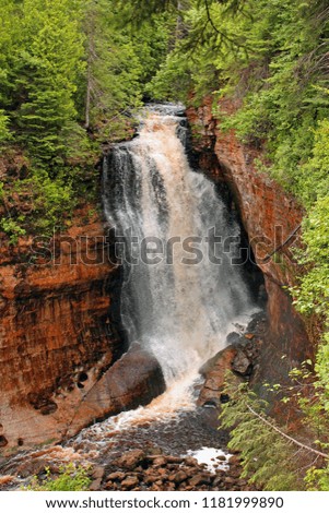 A flooded stream rushes over a waterfall in a lush forest in the Upper Peninsula of Michigan