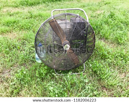 Large round powerful industrial professional metal iron fan with louvres for injecting air into the balloon against the background of green grass.