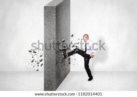 Businessman breaking wall of obstacle by kick. Business challenge conquering adversity concept Royalty-Free Stock Photo #1182014401