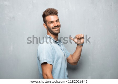 young handsome man with a satisfied, proud and happy look with thumbs up, signalining OK with one hand, sending a positive, "alright' message. Lateral or side view.