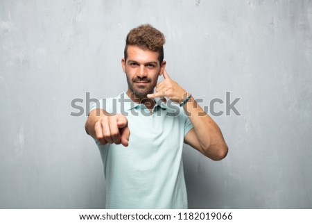 young handsome man making a phone call gesture or sign, with a proud, happy, satisfied look; offering communication with a smile, pointing forward towards you.