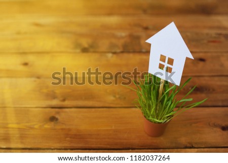 Paper models of house in pots with a green grass on a wooden background. Dreams of the house Royalty-Free Stock Photo #1182037264