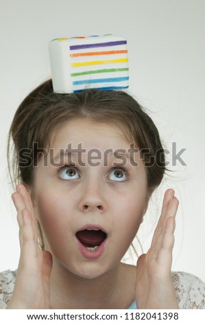 The picture of a eye-opened girl with surprised face expression and a squishy white cake on the bottom of her head over white backround   