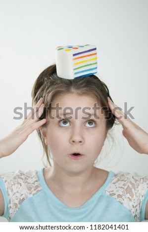 The vertical picture of a girl with a sguishy toy cake on her head and with a hands close to her temples over light background