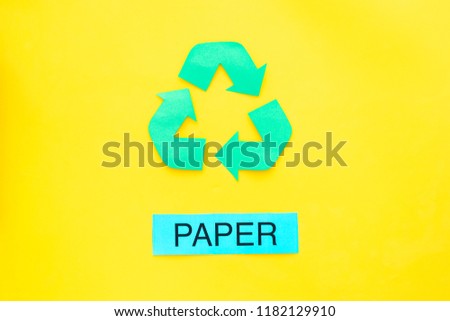 Types of matherial for reycle and reuse. Printed word paper near eco symbol recycle arrows on yellow background top view copy space