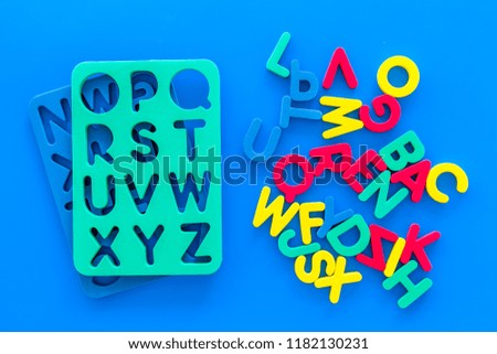 Alphabet for kids concept. English letters in disorder near stencil on blue background top view