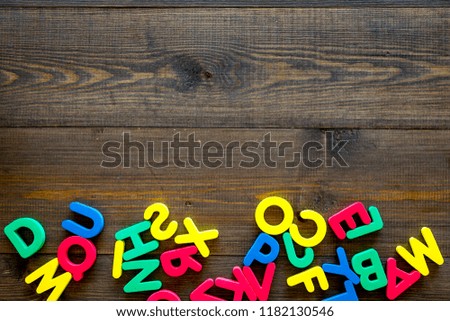 Alphabet for kids concept. English letters in disorder on dark wooden background top view copy space