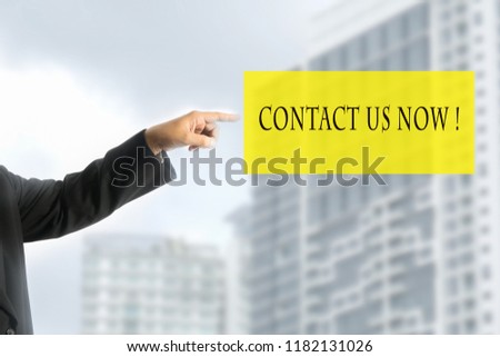 Concept or conceptual business on a male's finger with text CONTACT US NOW ! and blur building background.