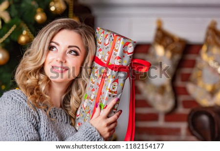 beautiful woman smiles and holds gift for New Year in her hand near head and poses for photo session on background of ?hristmas location. Close-up