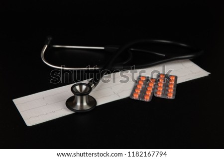 Medicine: stethoscope, electrocardiogram (ECG), pills and blisters pack on a black background.