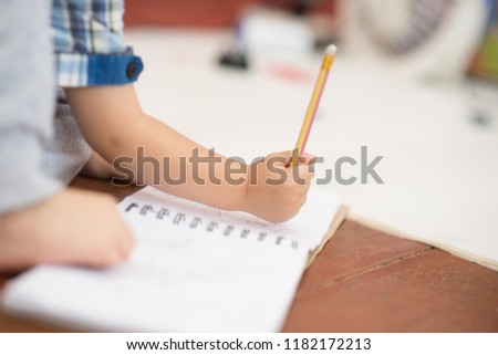 Little toddler boy draw pictures on a paper by use pencil