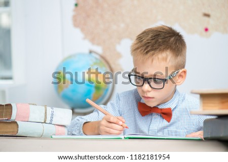 The schoolboy sits at his desk and writes in a notebook