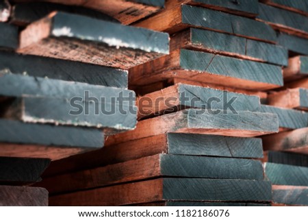 Stack of old fossil wood planks forming a solid wall. Orange and teal colors, long and slim oak slabs, ready for export and shipment in industrial carpentry facility. 