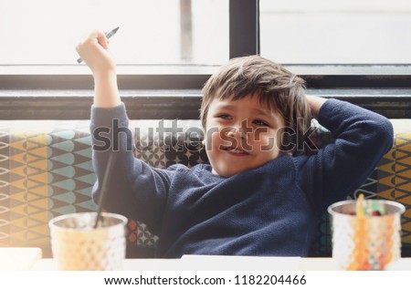 Happy kid boy showing crayon on his hands for colouring on paper while waiting for food in resturant.Selective focus of kid enjoy relaxing time with parent,Activity for children with family
