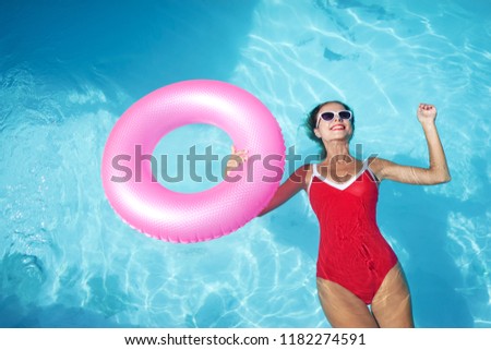 Enjoying suntan and vacation. Outdoor portrait of pretty young woman in red swimsuit with inflatable ring in swimming pool.