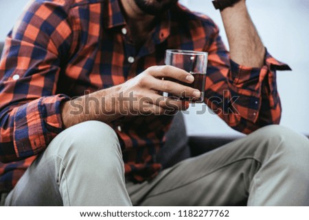 cropped shot of young man holding glass of whiskey while sitting on couch