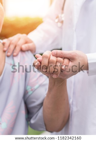 Elderly senior dementia patient (aging old adult person) in nursing hospice home holding geriatrician doctor's hand having happy medical health care from hospital carer or caregiver healthcare service Royalty-Free Stock Photo #1182342160