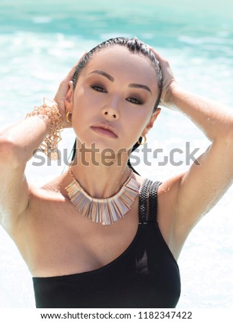young asian woman in a black swimsuit with juwels and wet hair in a pool