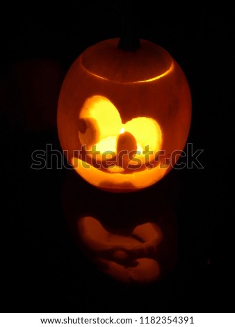 Funny little jack o lantern glowing in the dark, reflection, cartoon style. Halloween party, October 31, autumn season.
